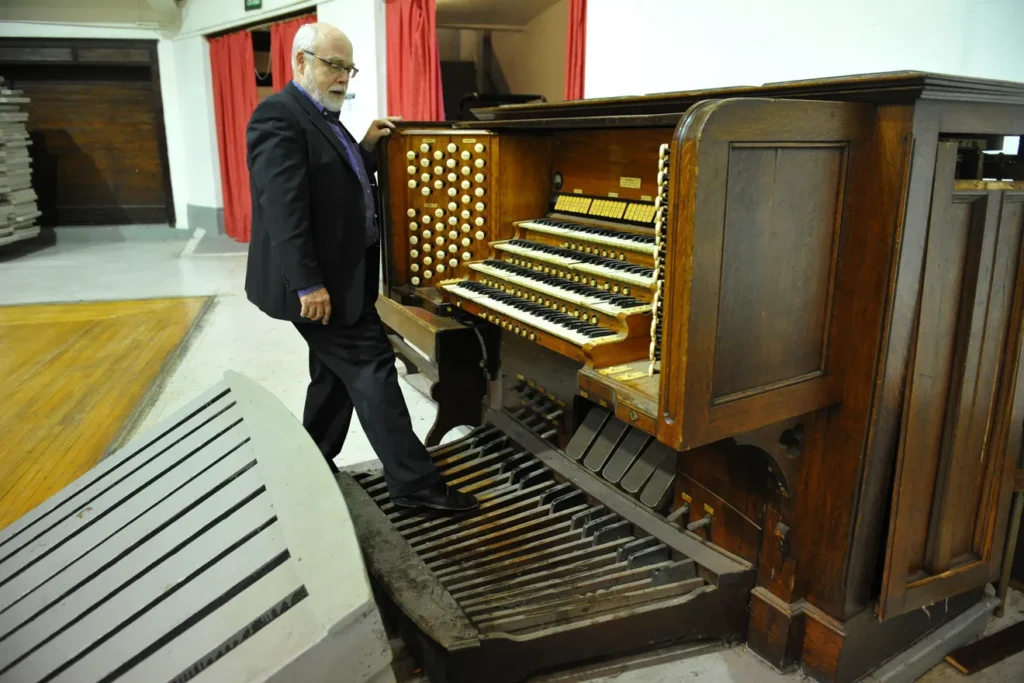 A man in a suit tests the pedals of a large wooden organ